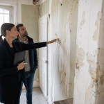 Deux personnes examinant un mur au papier peint abîmé